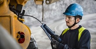 En tekniker, som smører en rammestyret Volvo dumper ved hjælp af en smørepistol.