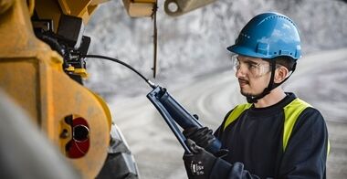 En tekniker, som smører en rammestyret Volvo dumper ved hjælp af en smørepistol.