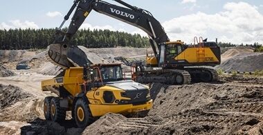 Un tombereau automoteur articulé Volvo A35 est chargé de matériaux  par une pelle hydraulique Volvo EC750 dans une carrière ou sur un chantier de construction