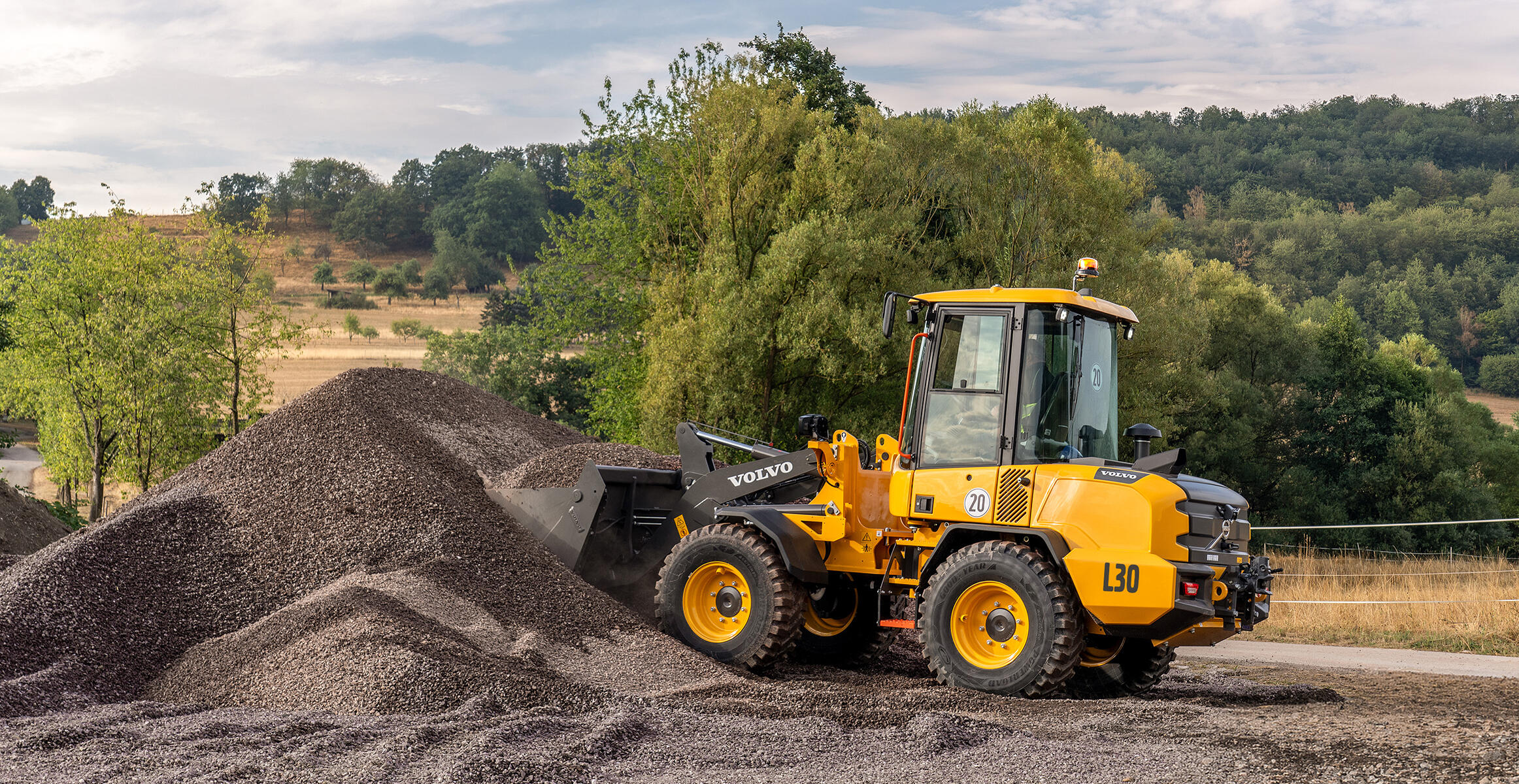 Volvo L30 Compact Wheel Loader working beside an aggregate pile on rough terrain.