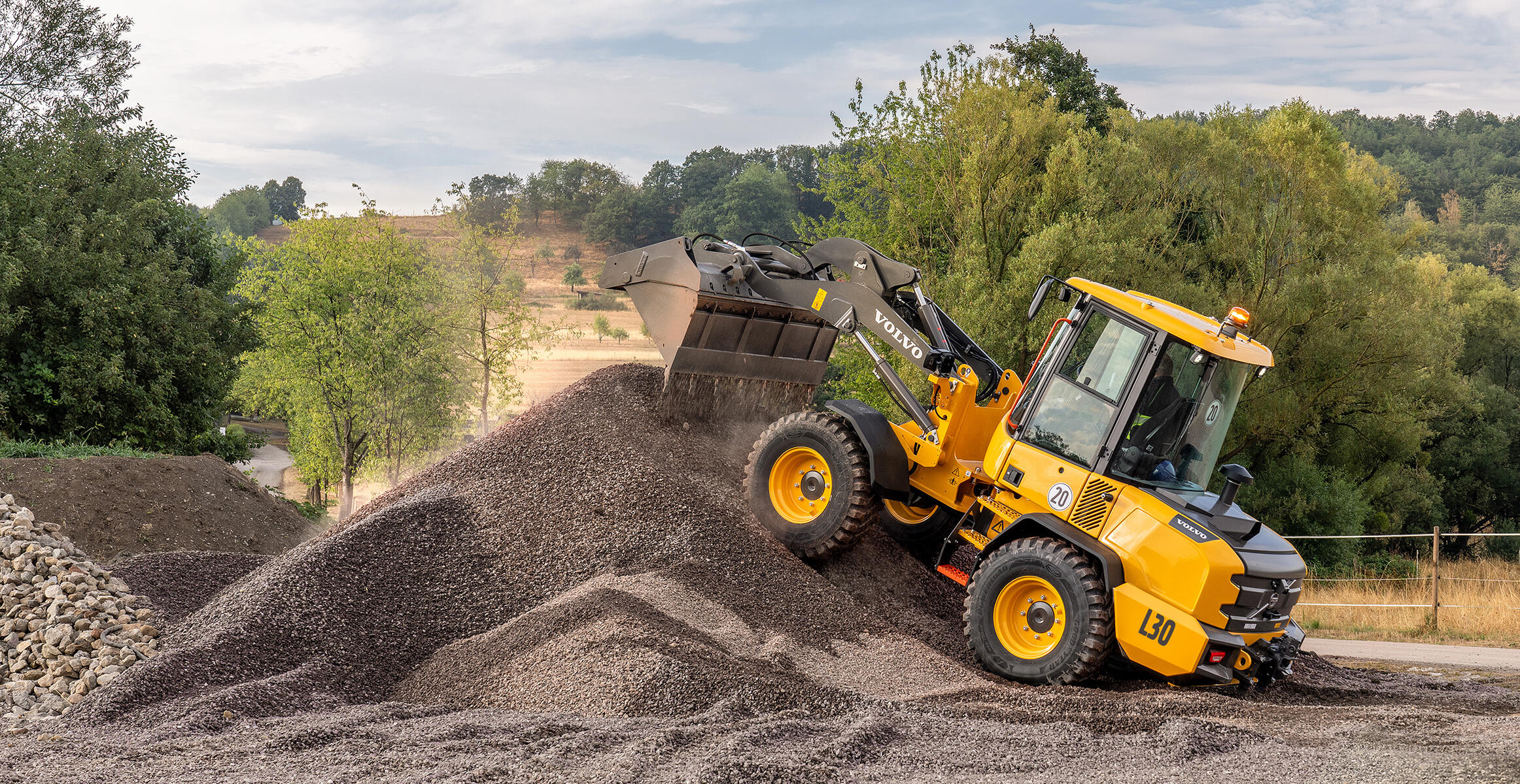 Volvo L30 Compact Wheel Loader driving over an aggregate pile on uneven terrain.