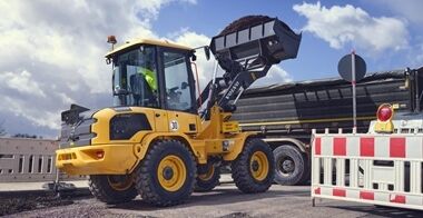 Vue arrière d'une chargeuse compacte sur pneus Volvo L30 L35 remplissant un camion à benne basculante avec des matériaux.