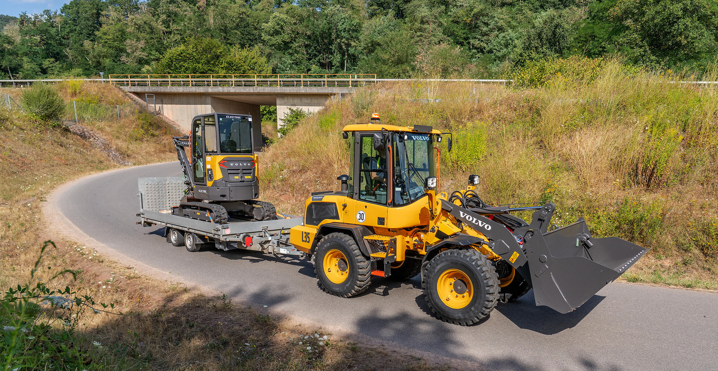 Volvo L35 Compact Wheel Loader towing a trailer carrying a compact excavator.