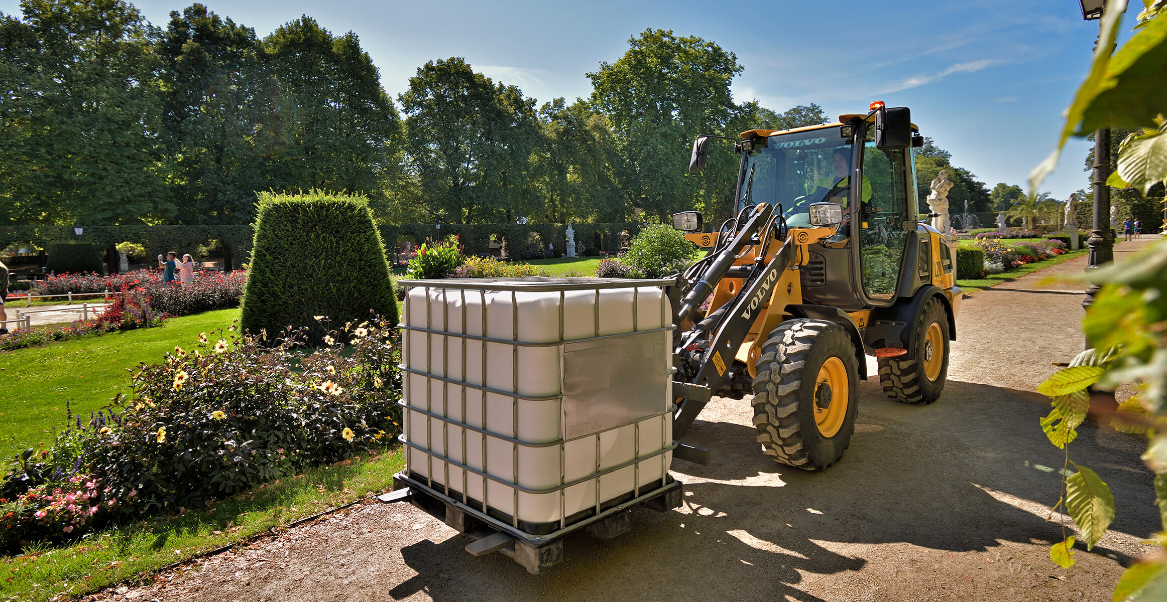 Elektryczna kompaktowa ładowarka kołowa Volvo L20 Electric przewożąca na palecie zbiornik na wodę przy użyciu osprzętu z widłami w ogrodzie