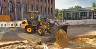 Volvos kompaktlastare L20 Electric tömmer en skopa med sand på en byggarbetsplats i stadsmiljö