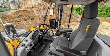 Volvo L120 Electric wheel loader dumping grayish-brown aggregate from raised bucket into a in a gravel quarry.