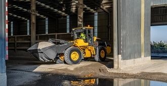 Side view of a L120 electric wheel loader moving gravels into a depot building.