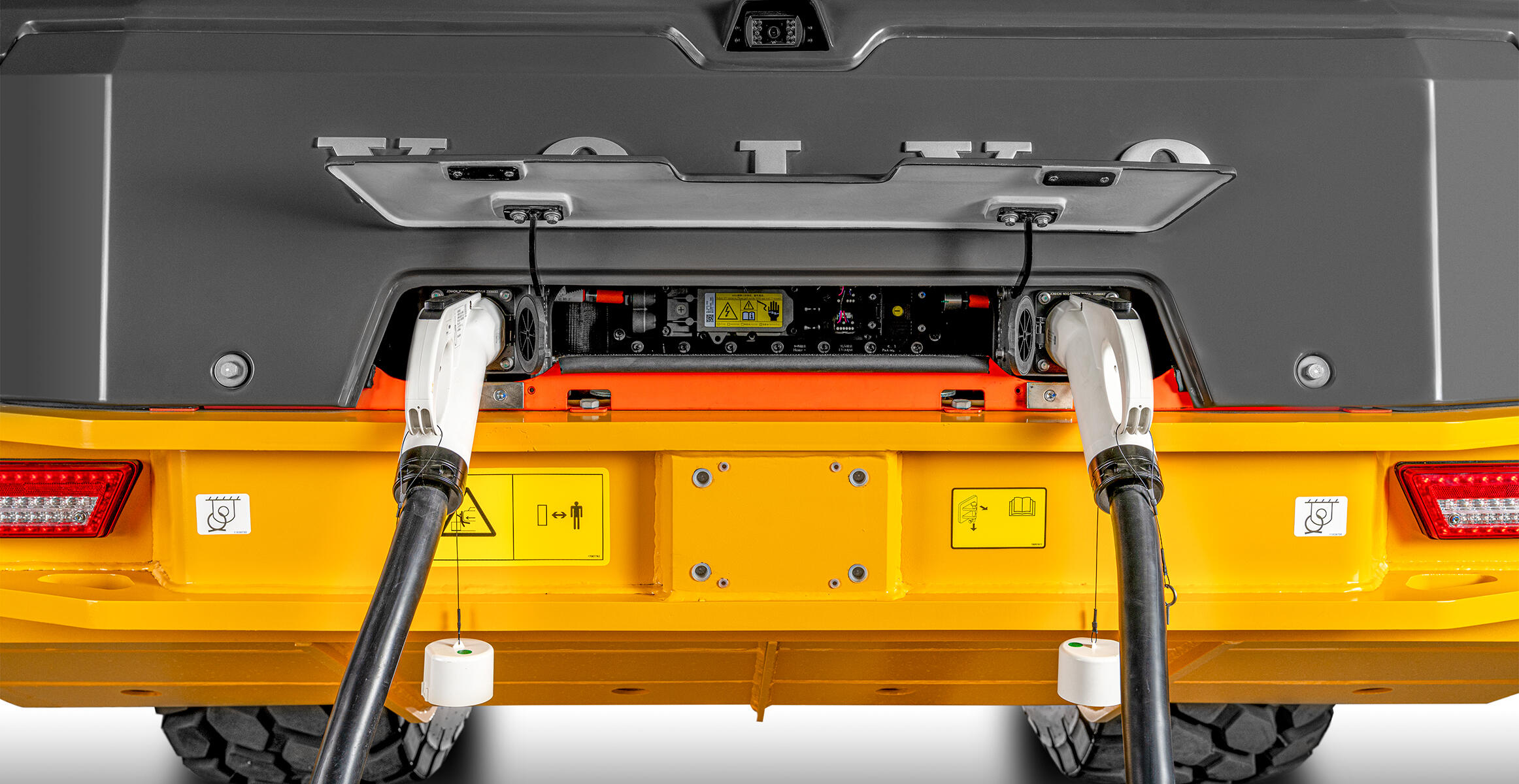 Close-up of the Volvo L120 Electric Wheel Loader's rear charging compartment with lid open, showing two plugged-in charging cables.