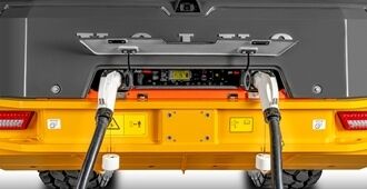 Close-up of the Volvo L120 Electric Wheel Loader's rear charging compartment with lid open, showing two plugged-in charging cables.
