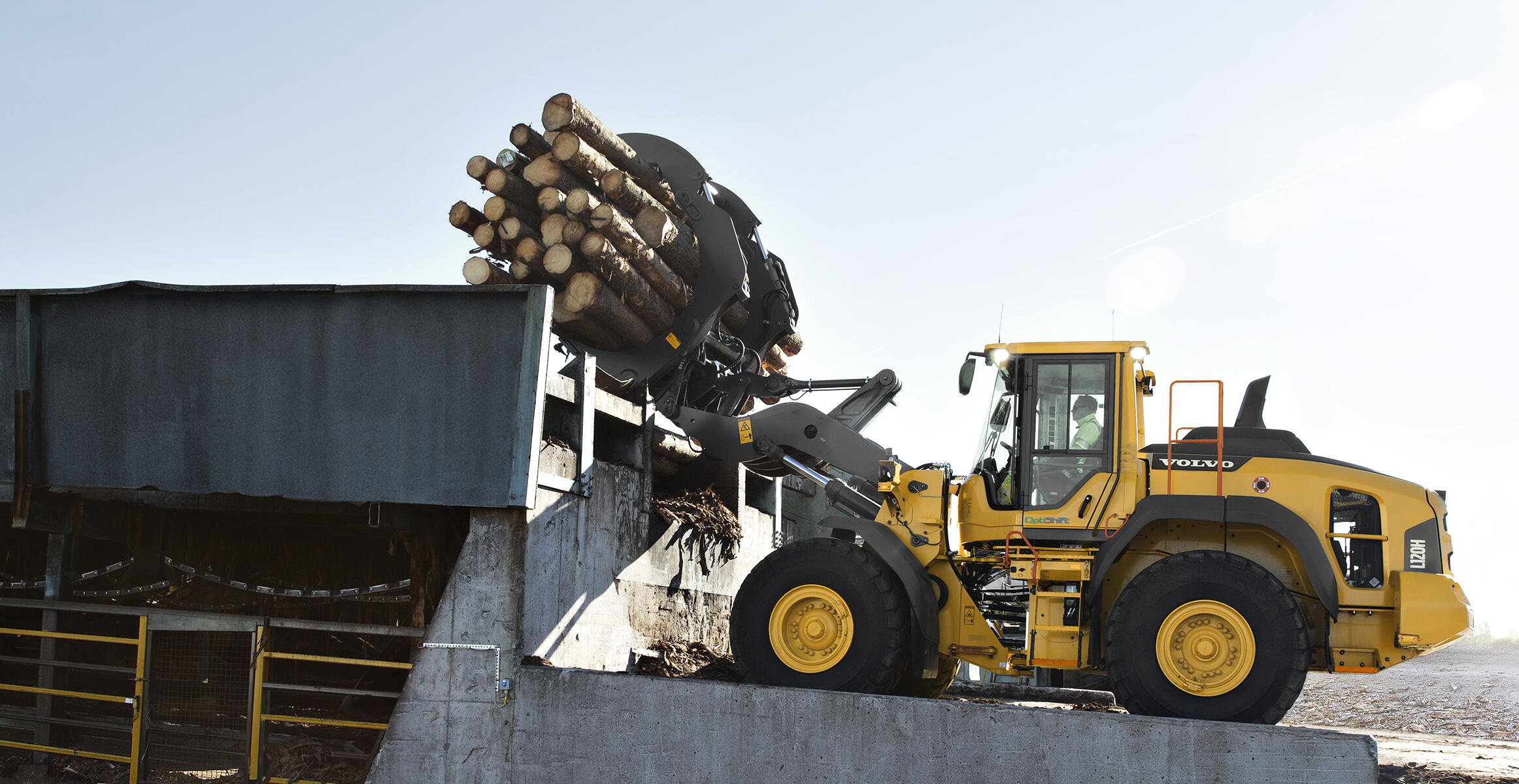 Side view of a L110H or L120H Volvo wheel loaders moving woods with a log grapple.