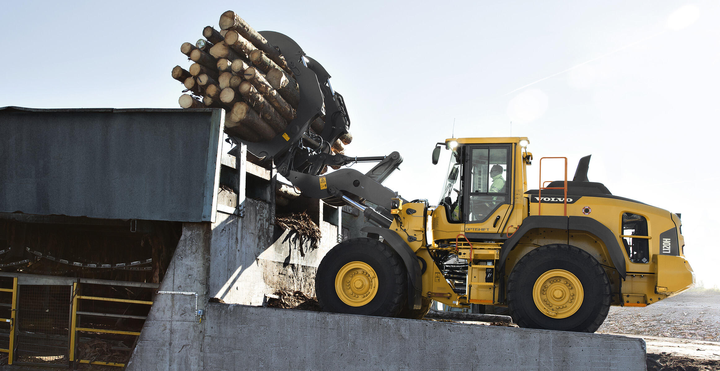 Side view of a L110H or L120H Volvo wheel loaders moving woods with a log grapple.