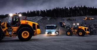Volvo L150-hjullastare och Volvo L180-hjullastare lastar en Volvo FMX-lastbil på natten i en bergtäkt