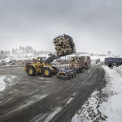 Side view of Volvo L350H loading with log grapples timbers in a long haul truck during winter.