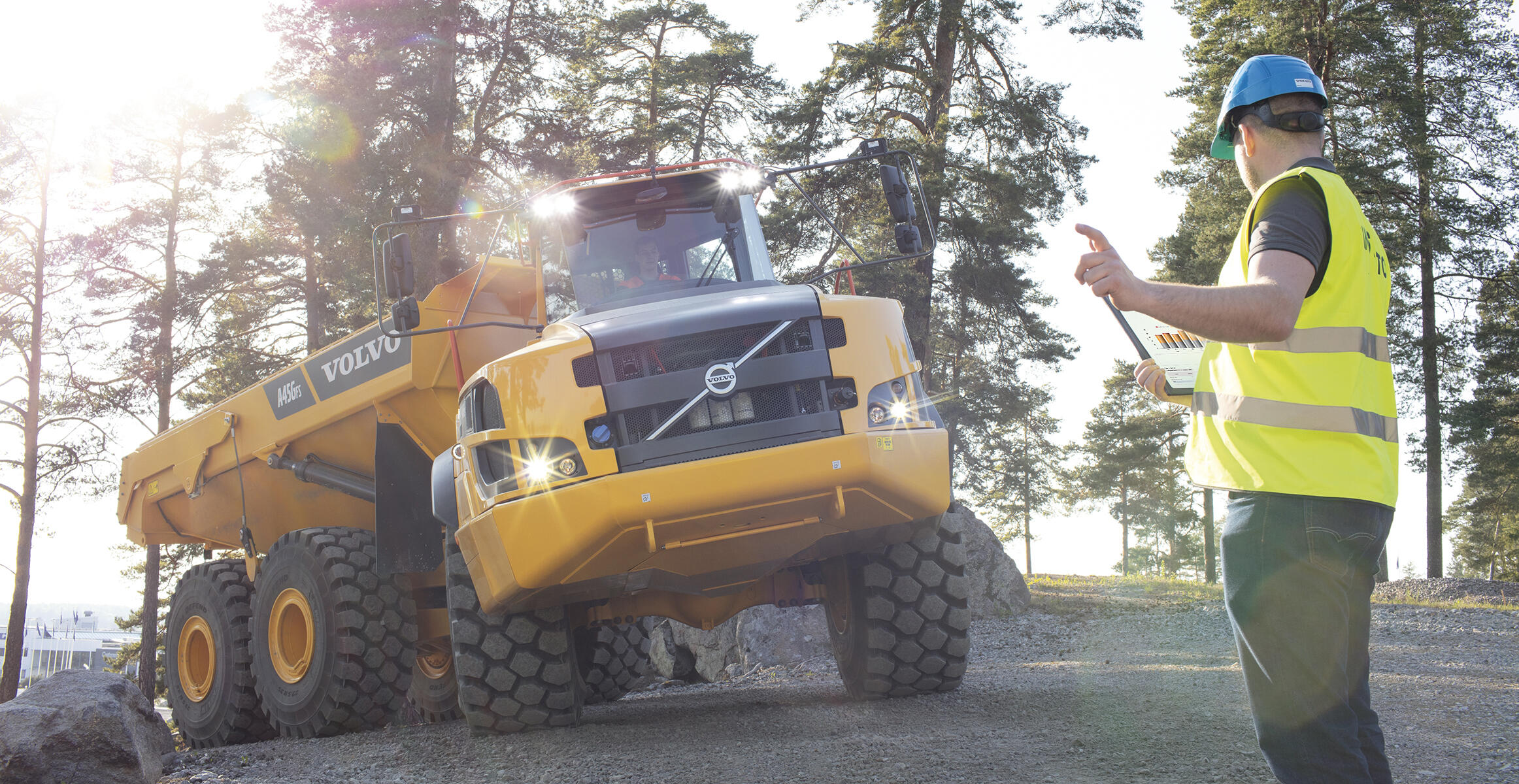 Worker directing Volvo articulated hauler on construction site with tablet device