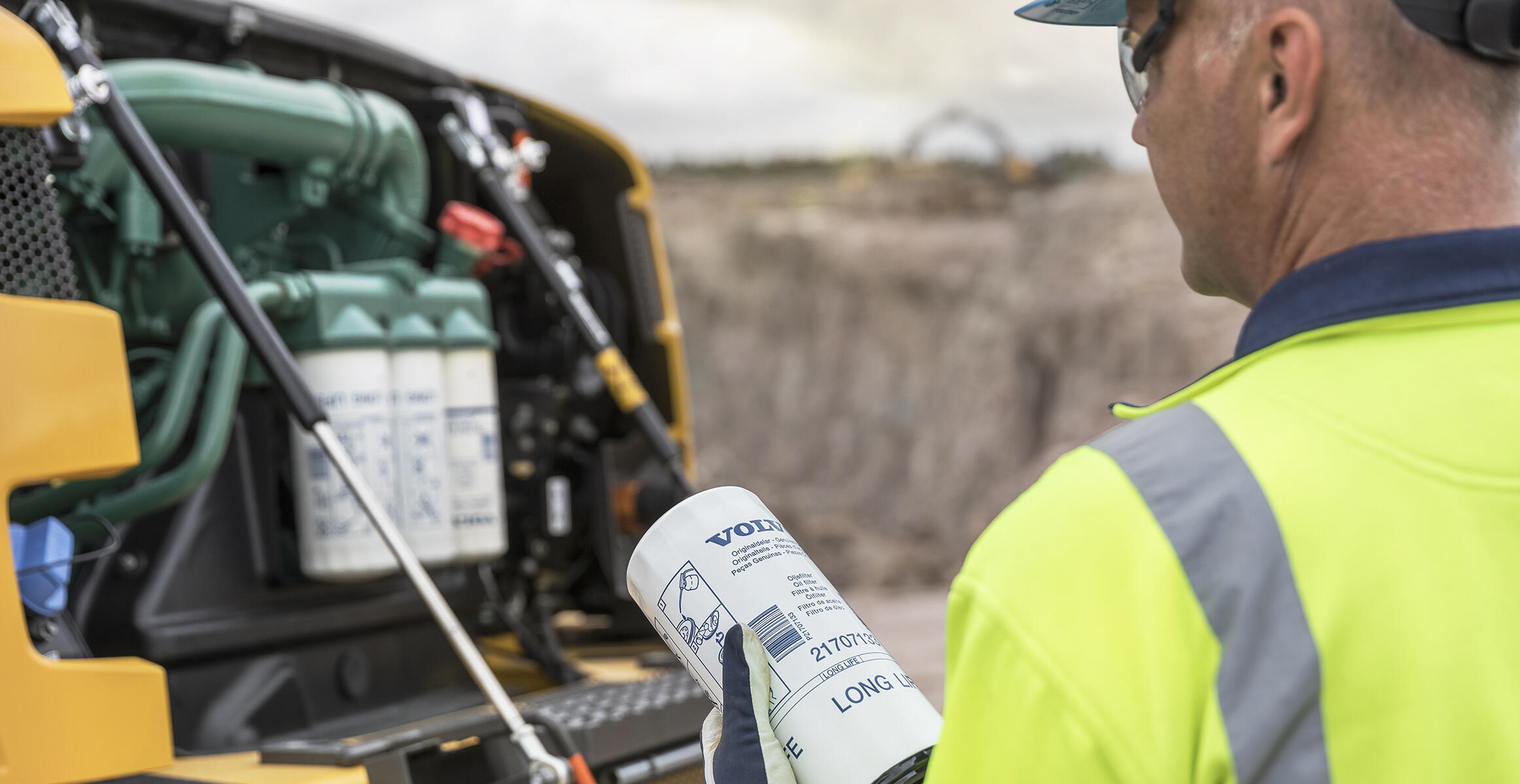 Technician holding Volvo filter while inspecting construction equipment engine compartment at jobsite