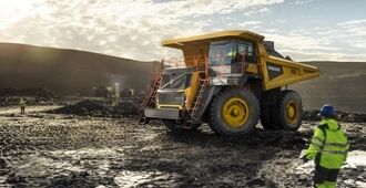 R100 rigid hauler arriving at a mining site, with two mine site managers giving arm signals to guide the truck driver for precise positioning and safe operation.