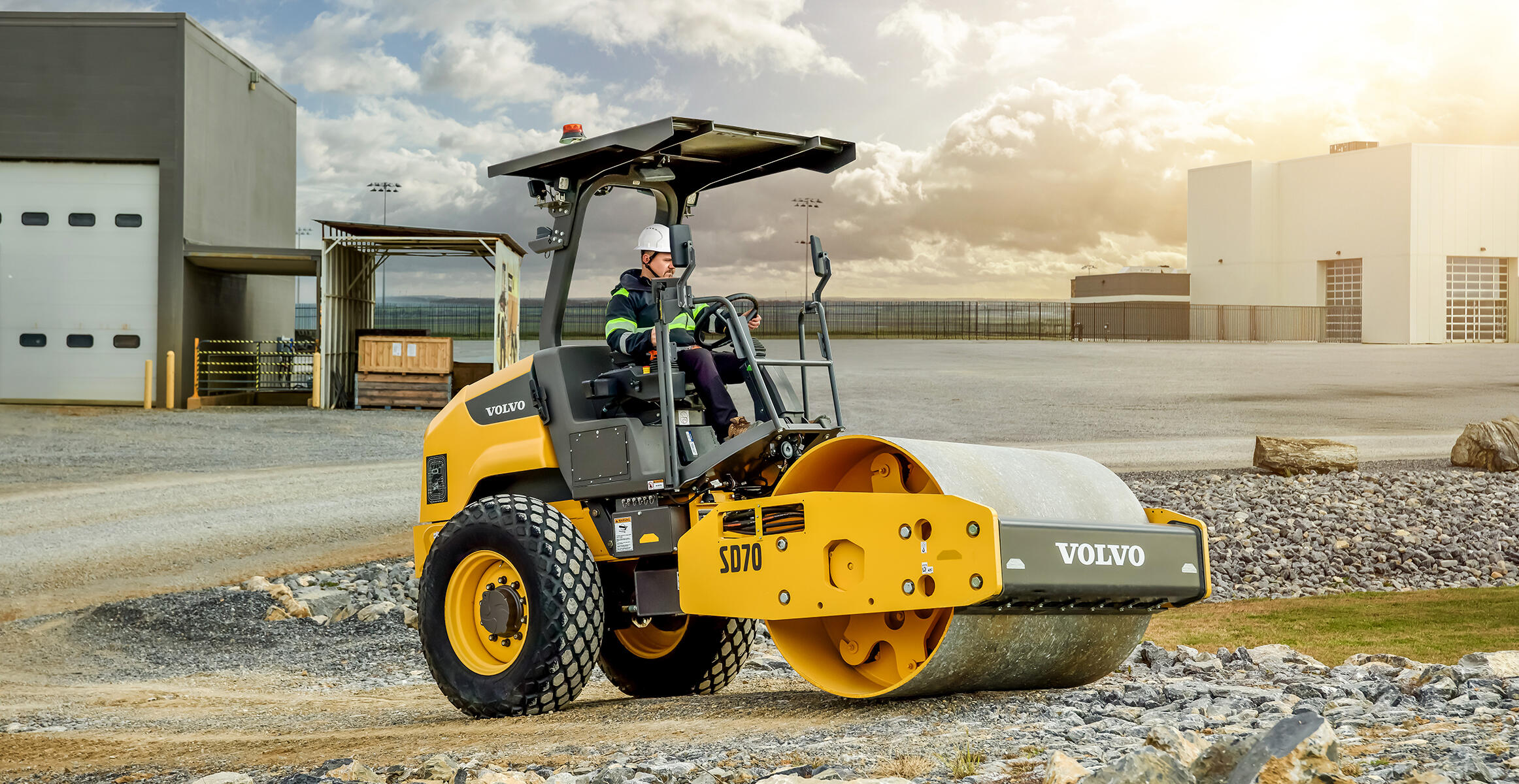 Side view of a Volvo SD70 soil compactor in front of industrial buildings