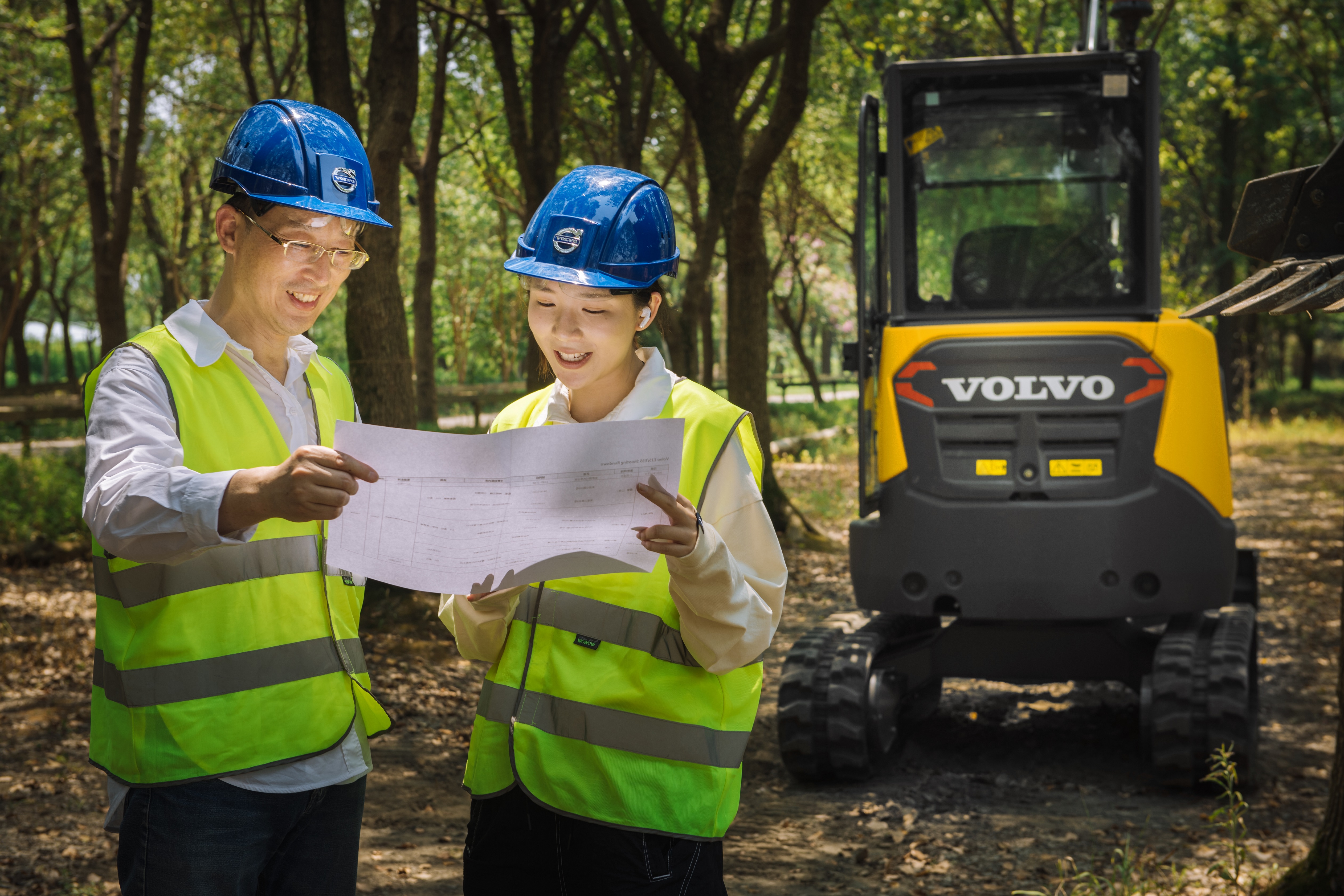 Two operators smiling in the forest with Volvo machine behind them