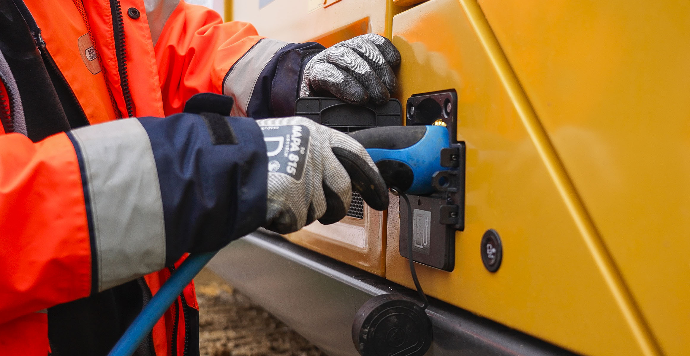 Electric excavator being plugged into charging by an operator.