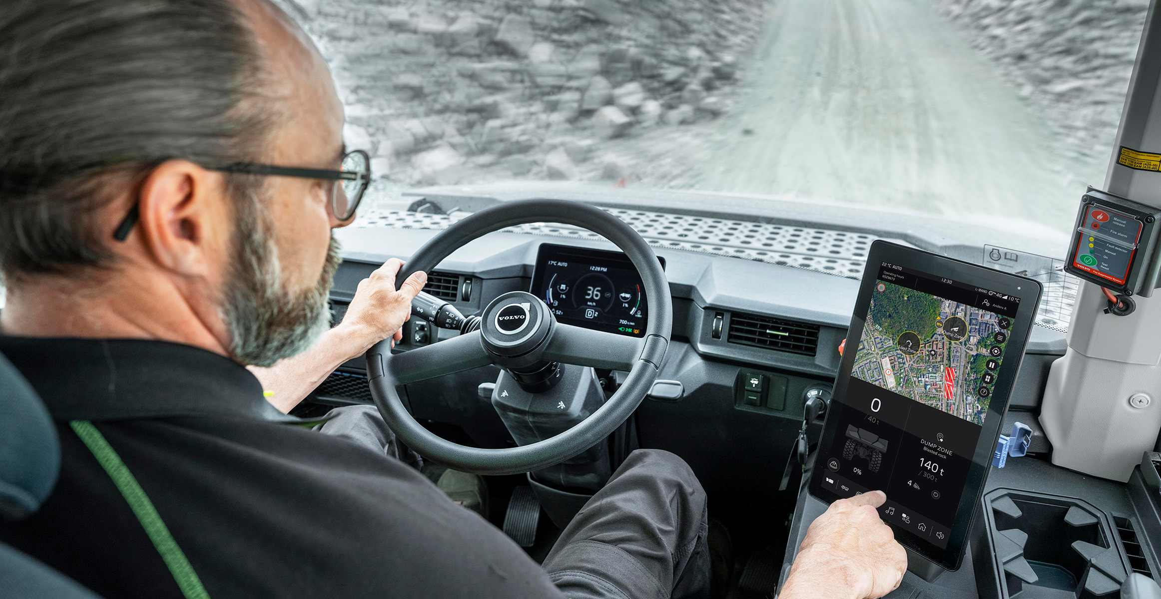 Förare som kör Volvos ramstyrda dumper på en grusväg, sett inifrån hytten.