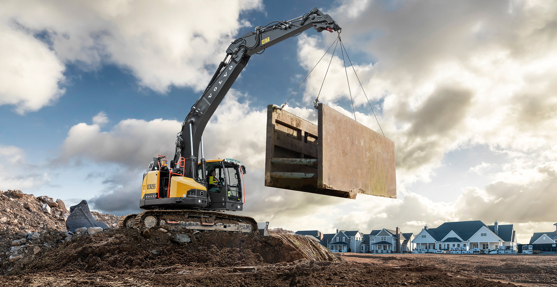 Volvo CE ECR255 crawler excavator lifting concrete block against cloudy sky on construction site