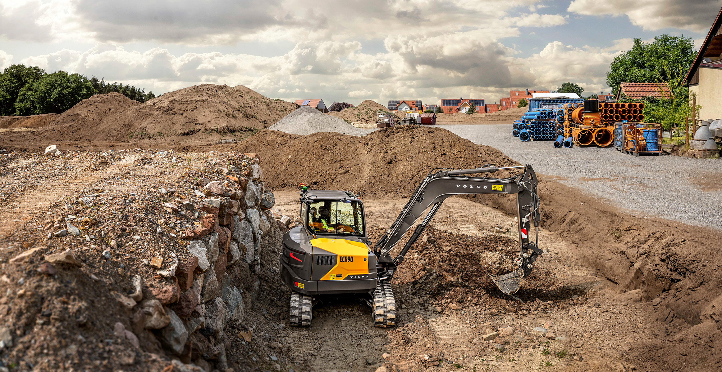 Volvo compact excavator working at construction site with soil piles