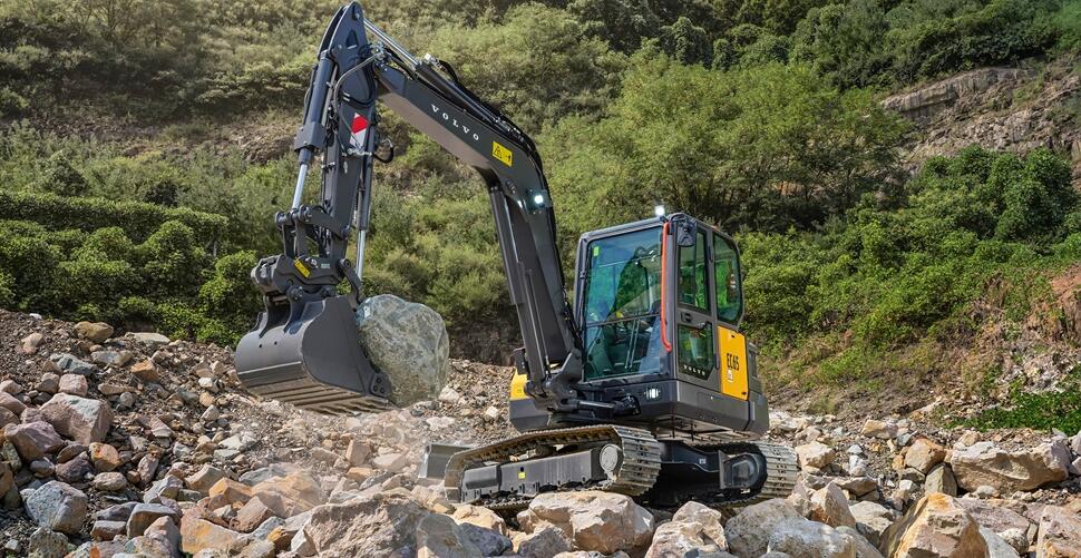 Volvo tracked excavator on rocky hillside with forest background