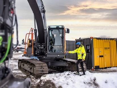 Maskinförare som övergår till eldrift genom att använda en stor eldriven grävmaskin och en mobil laddningsenhet på en byggarbetsplats.
