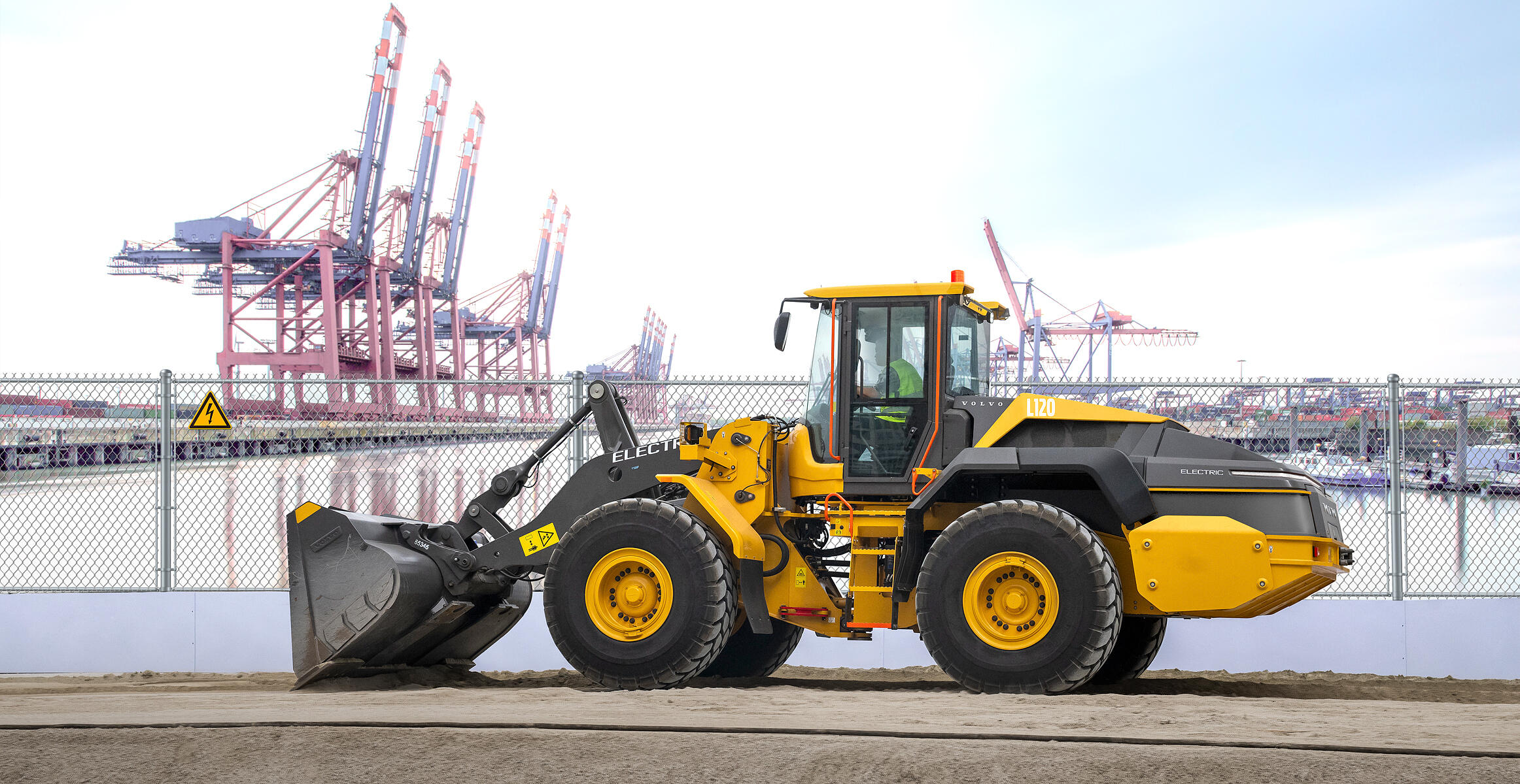 Volvo electric wheel loader working in harbour with large cranes.