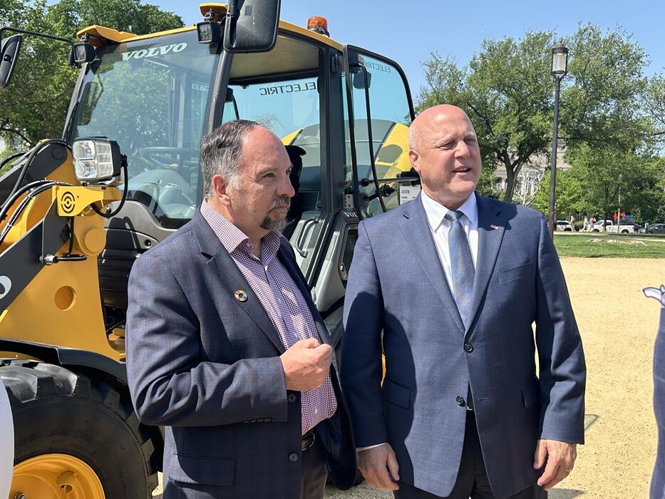 two men in suits standing in front of a volvo machine