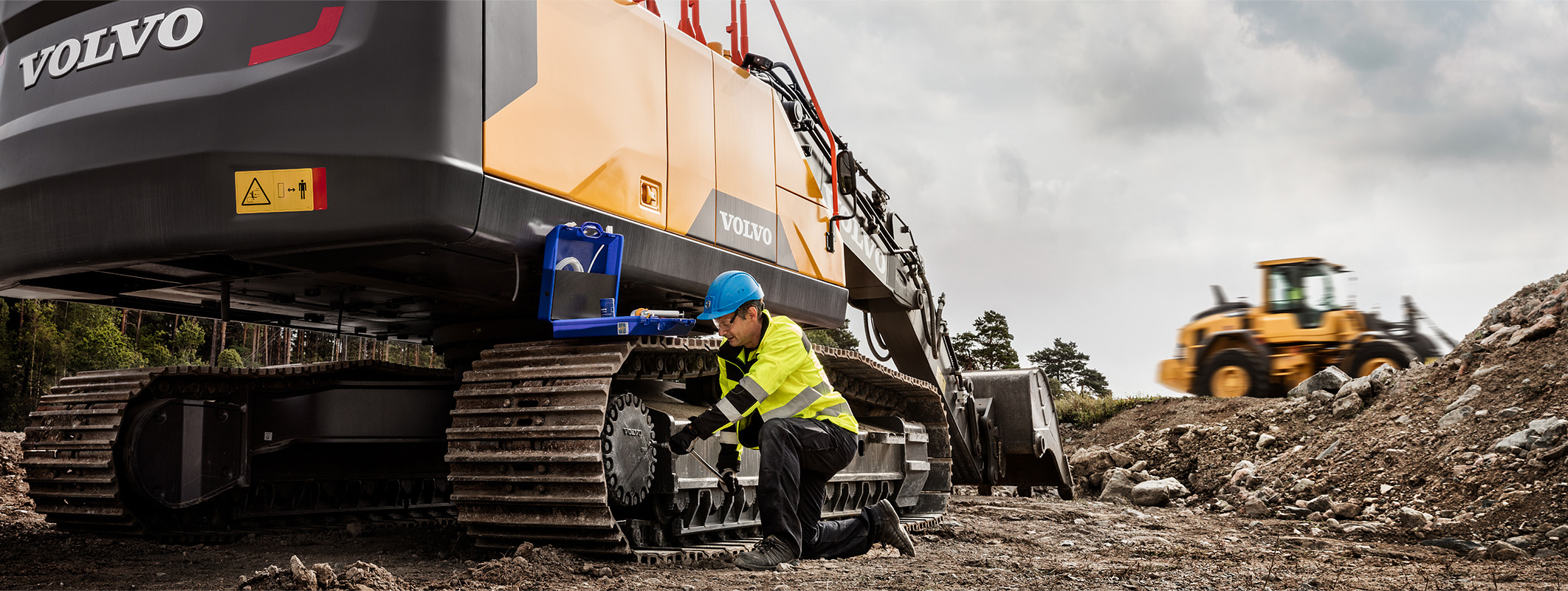 Technician performing maintenance on Volvo excavator tracks at construction site