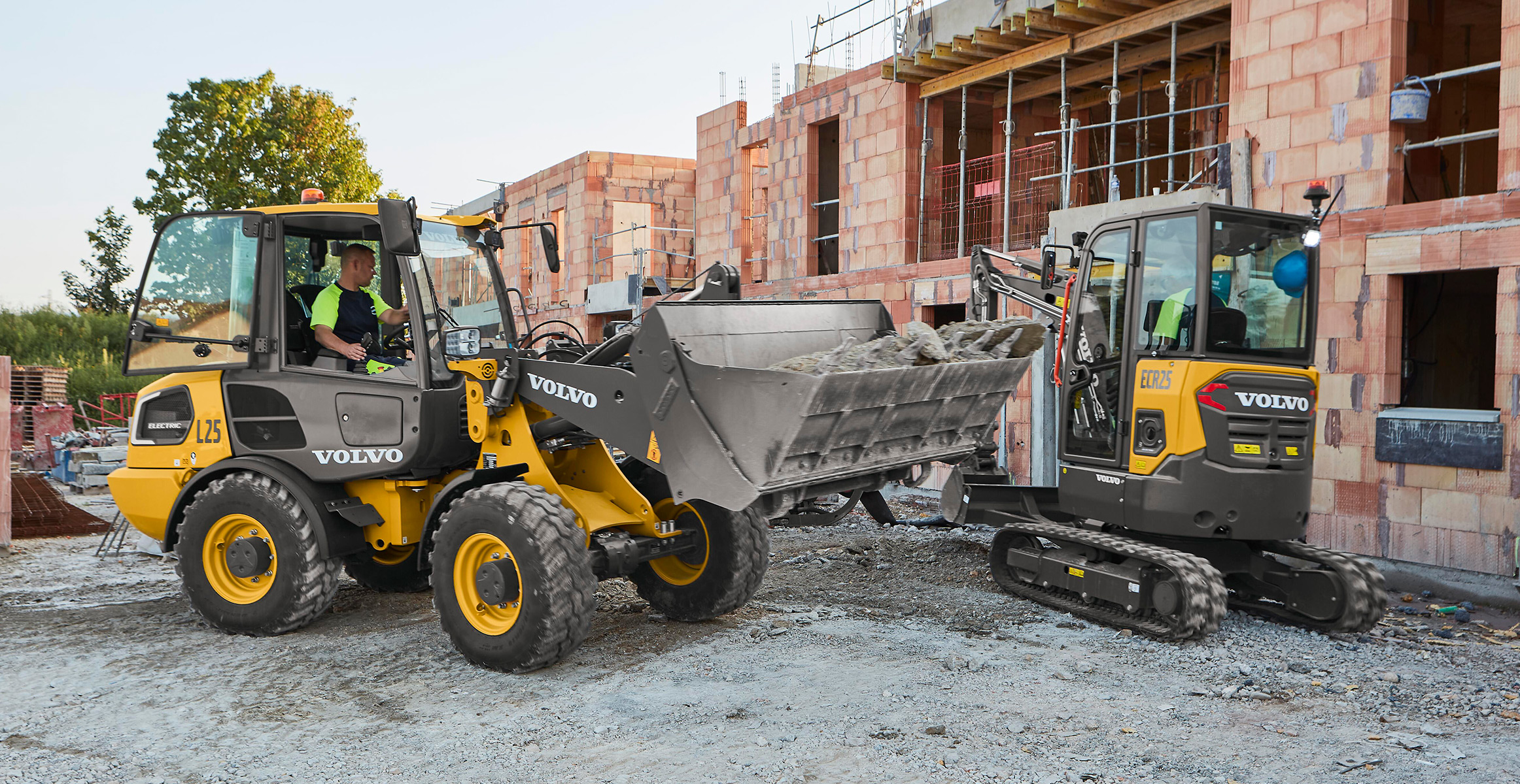 A Volvo electric wheel loader and electric excavator working together in construction.