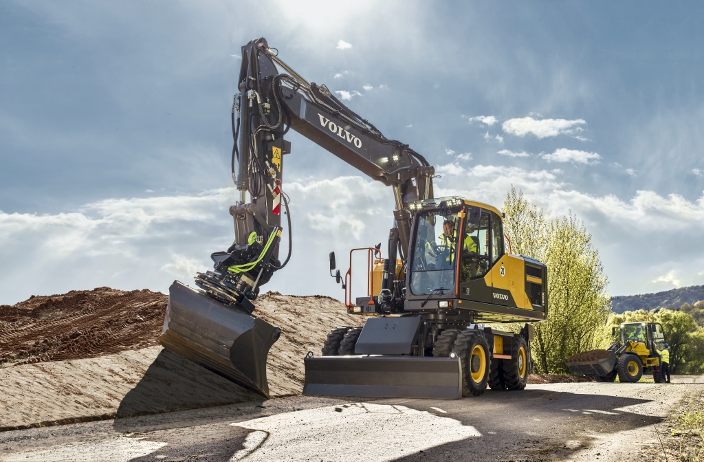 Volvo wheeled excavator angling dirt next to a road with a tiltrotator and bucket.