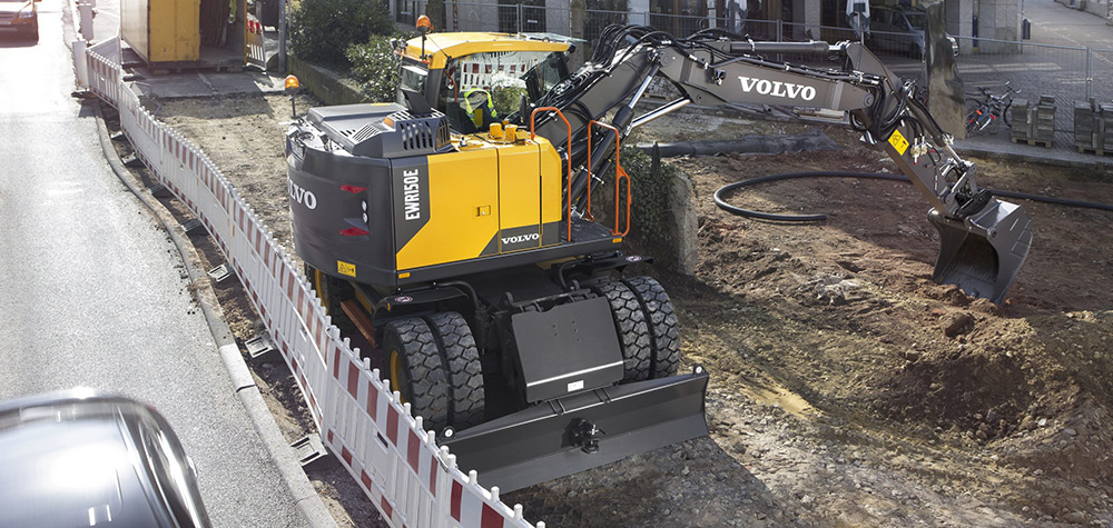 Volvo wheeled excavator digging trenches in a residential area in utilities.