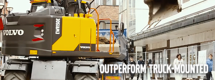 Volvo wheeled excavator slewing on an urban construction jobsite with pedestrians safely walking by.