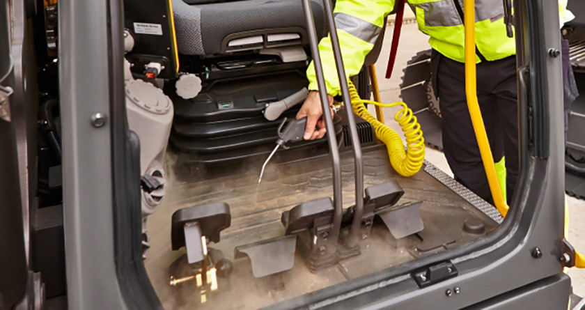 An operator blowing out the cab of a Volvo excavator with a compressed air hose.