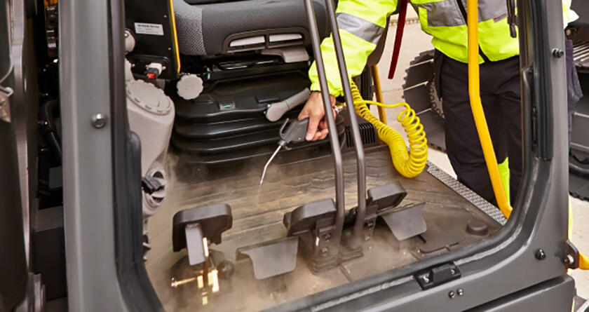 An operator blowing out the cab of a Volvo excavator with a compressed air hose.