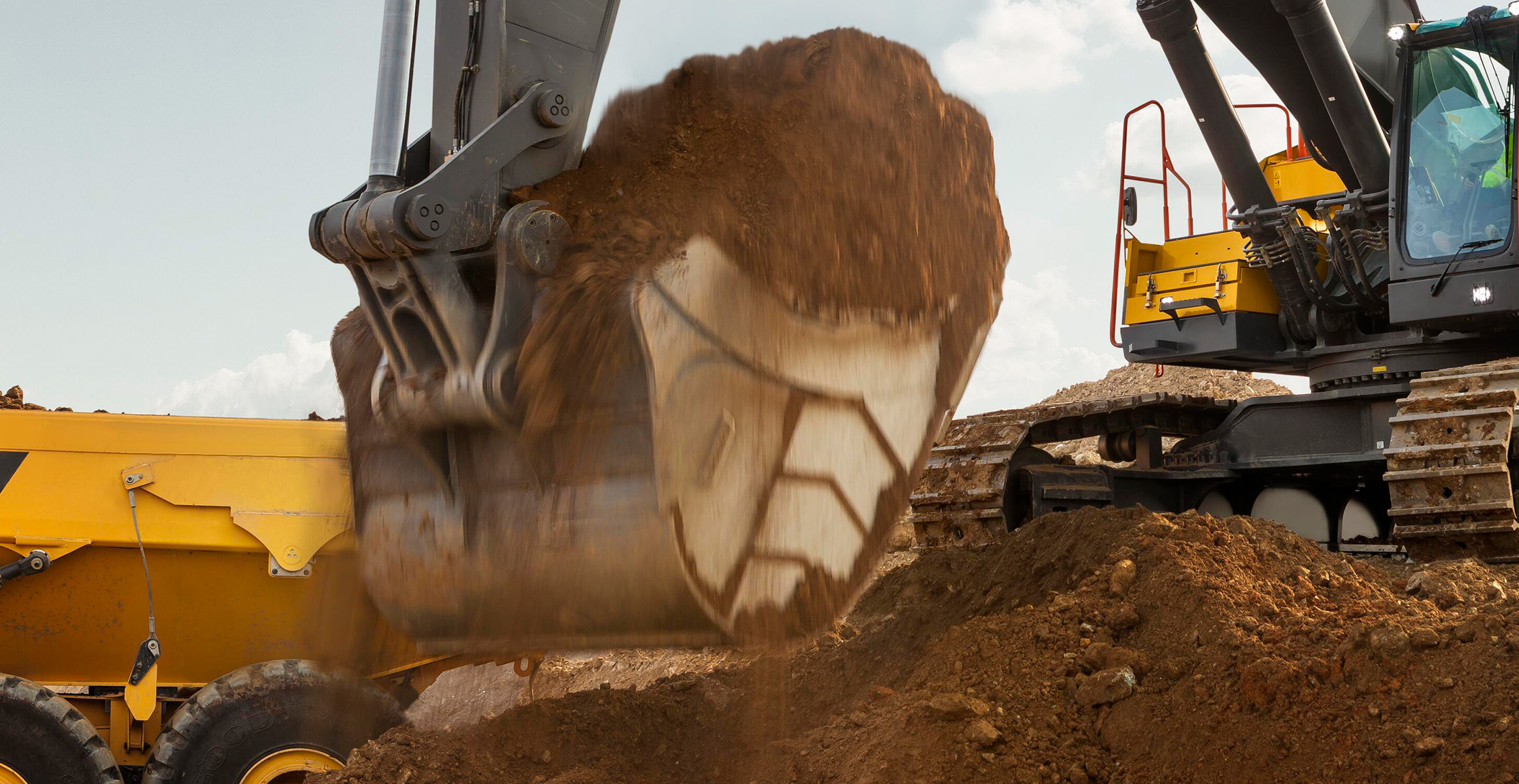 Close-up of a Volvo excavator bucket scooping dirt that’s being loaded into a Volvo articulated dump truck.