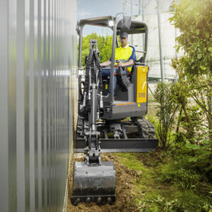 Volvo compact excavator trenching next to a building.