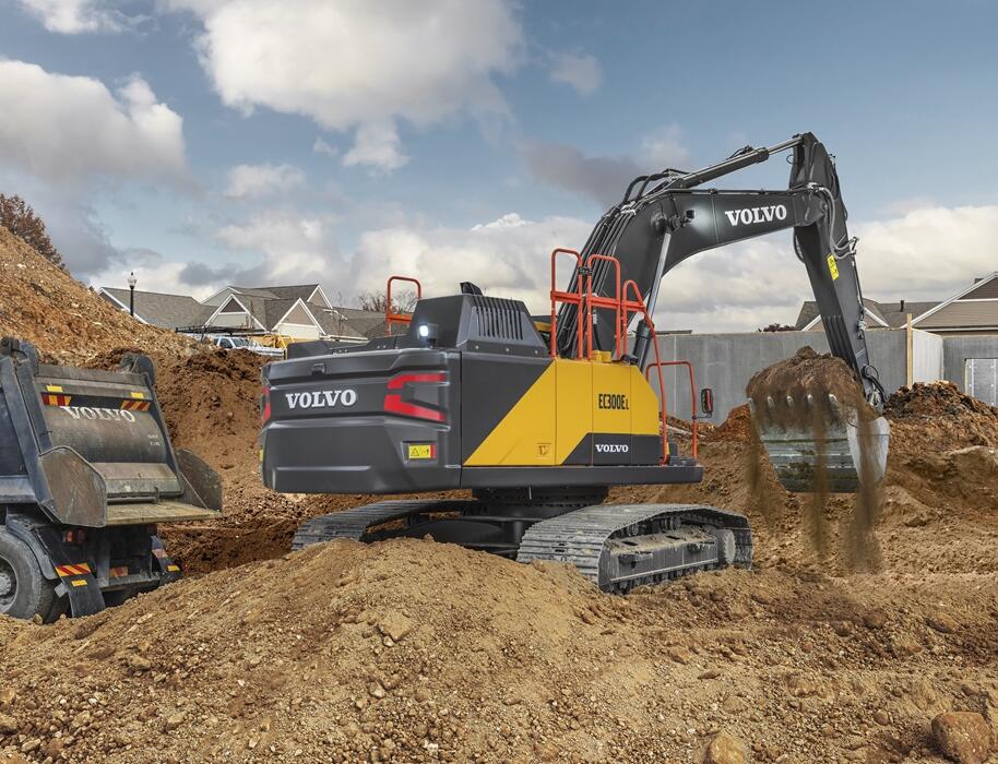 Volvo excavator loading dirt into a truck on a residential construction site.