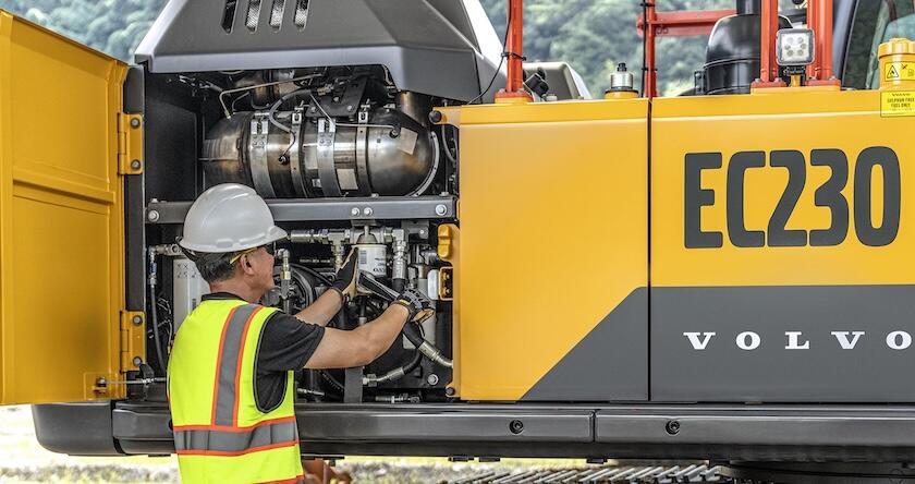 A construction equipment service tech changing a filter on a Volvo crawler excavator.