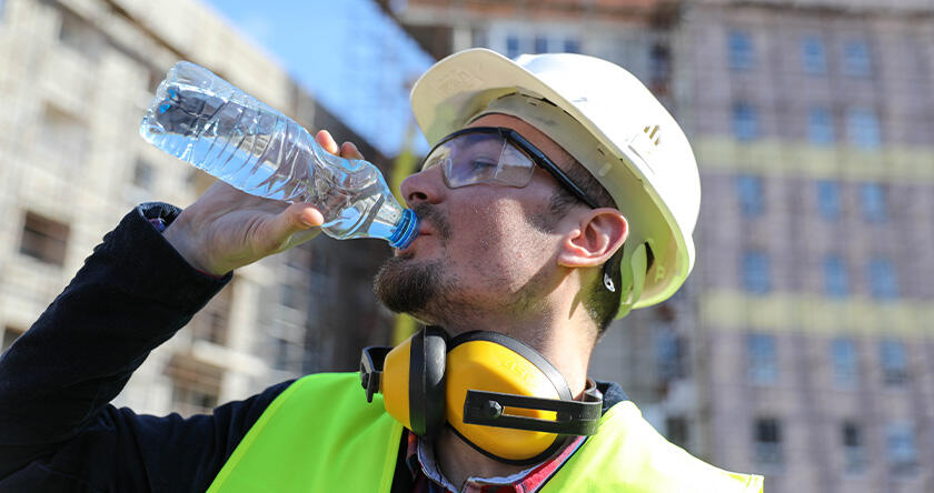 A construction worker staying hydrated by drinking water on a jobsite.