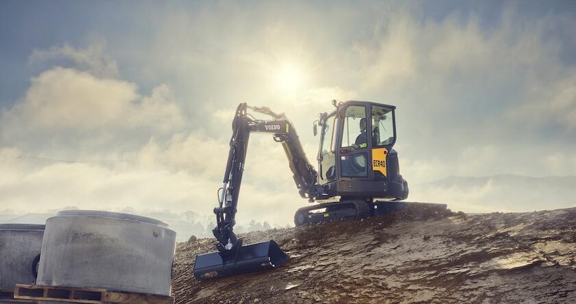 A Volvo compact excavator grading dirt in the summer sun.