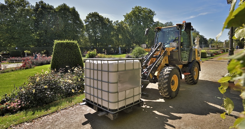 A Volvo L20 Electric wheel loader moving a pallet of material in a landscaped garden area.
