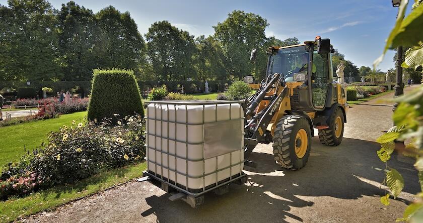 A Volvo L20 Electric wheel loader moving a pallet of material in a landscaped garden area.