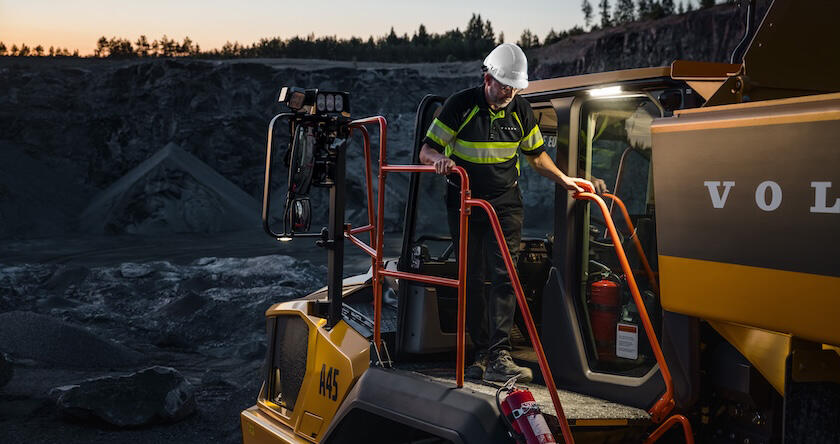 Un conducteur sortant de la cabine en utilisant les mains courantes orange d'un nouveau tombereau articulé Volvo.