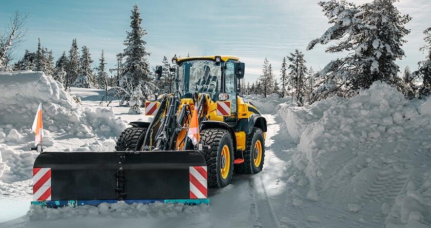 A Volvo wheel loader pushing snow to clear a road in winter.