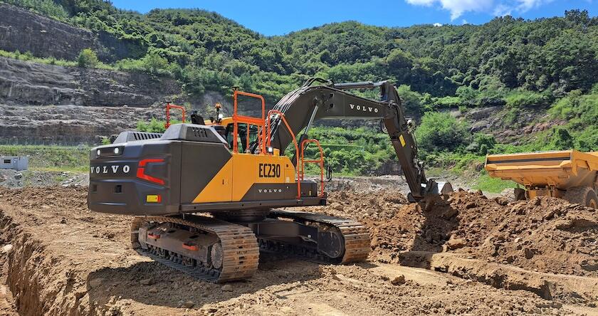 A Volvo EC230 crawler excavator loading dirt into an articulated dump truck.