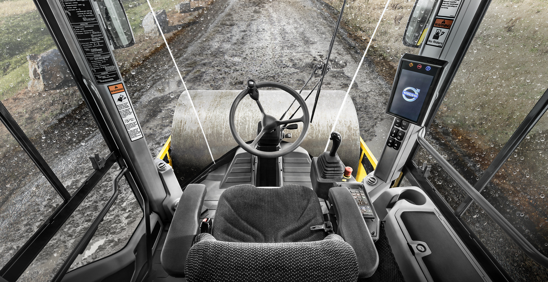 View out of a Volvo SD115B soil compactor cab with rain on the ground and windows.