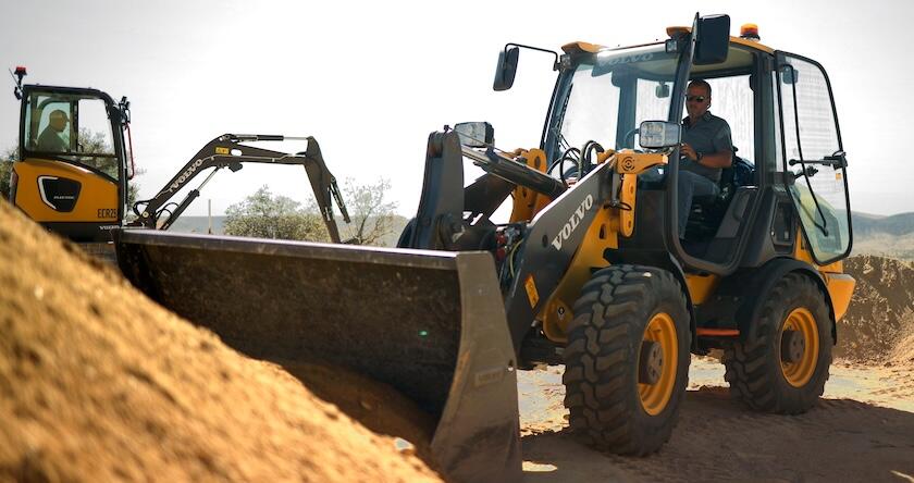 A Volvo electric excavator working with a Volvo electric wheel loader in residential construction.